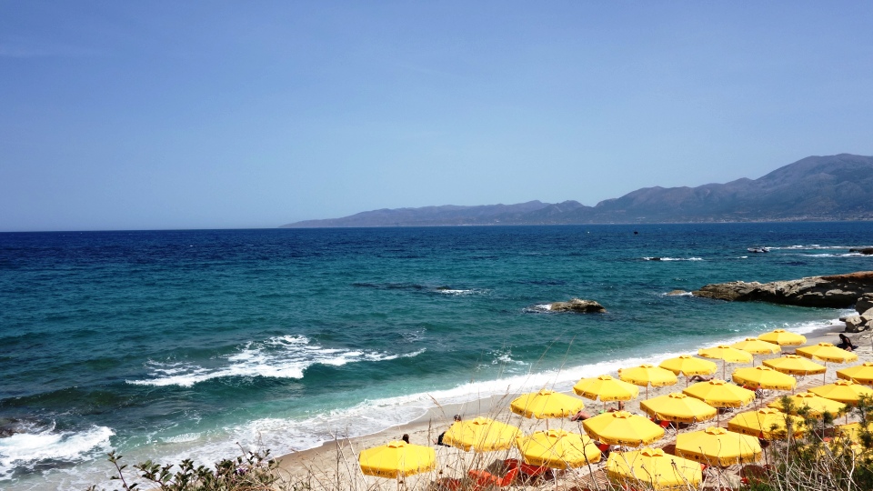 tourist sunbathing during their spring vacations under yellow umbrellas at Limanakia beach